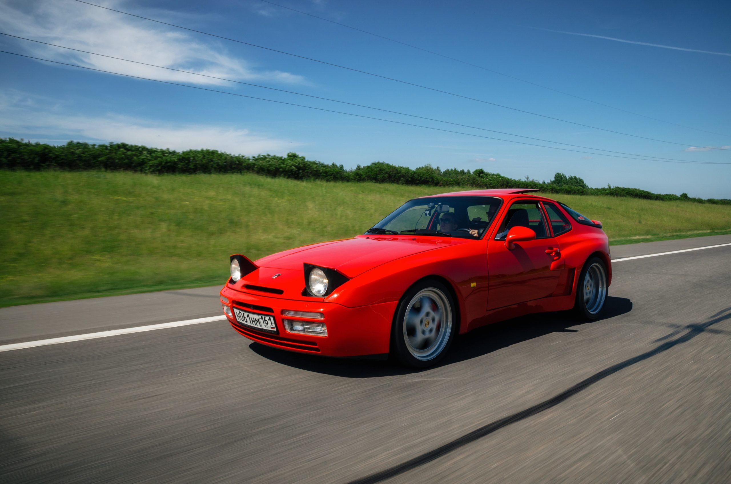 Red vintage Porsche 944 sports car speeding along road with motion blur effect.